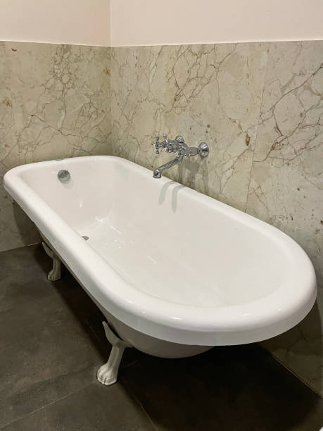 istock Image of luxury bathroom suite with Victorian style, white ceramic freestanding curved roll top bath with claw feet, chrome, wall mounted mixer tap, stone wall and floor tiles, elevated view, focus on foreground 1577204872