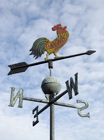 Black metal frame with a direction arrow, weathercock and east and ovest directions on a roof in the Chianti Classico Gallo Nero region.