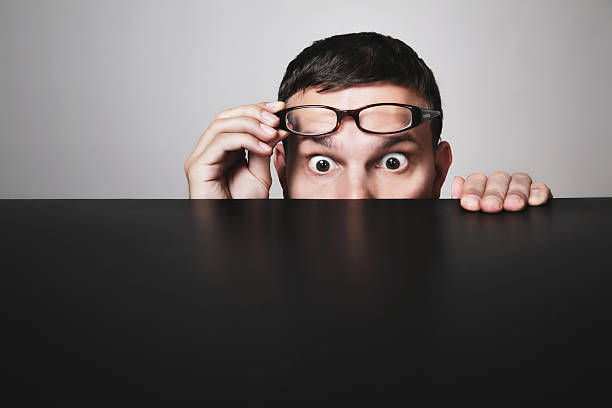 WTF curious young man looking over a table. a little bit scared maybe. with space for your copytext and scaring stuff. Hidden Meaning stock pictures, royalty-free photos & images