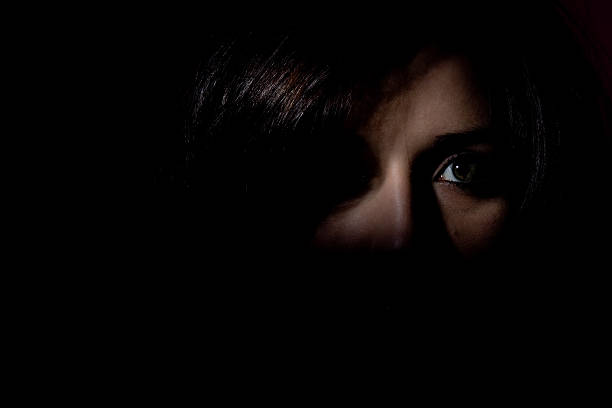 Woman stood in the dark showing half her face looking scared stock photo