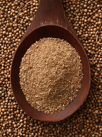 Top view of wooden spoon full of ground coriander seeds