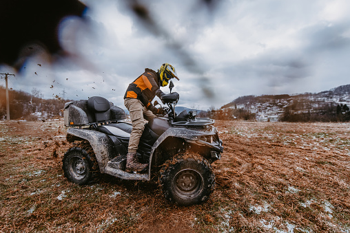A man is fearlessly enjoying an adventurous ride on an ATV Quad through hazardous snowy terrain, embracing the thrill and excitement of the challenging mountainous landscape.
