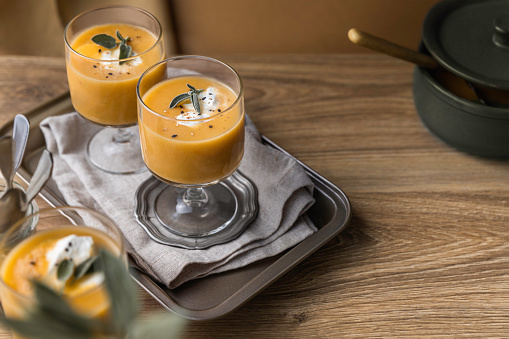 Orange vegetable creamy soup served in glasses on wooden table