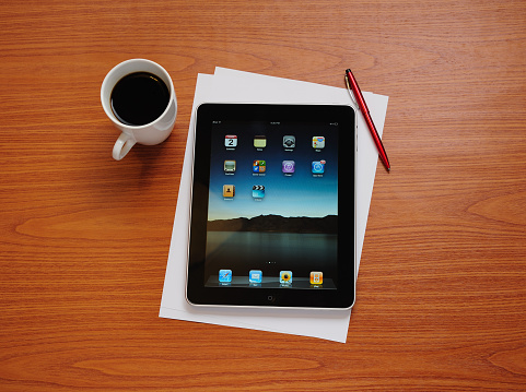 Digital tablet with wireless keyboard, smartphone and cup of coffee on wooden table.