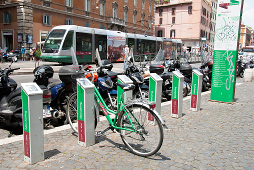 Rome, Italy - June 6, 2011: Bike sharing stand with bicycle. In the background is a tram, mopeds and people.
