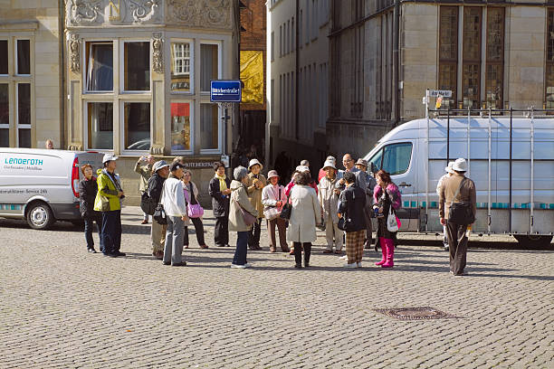 A lively outdoor café scene with people enjoying drinks and meals in front of a beautiful cathedral in Aachen. The atmosphere is relaxed and social.