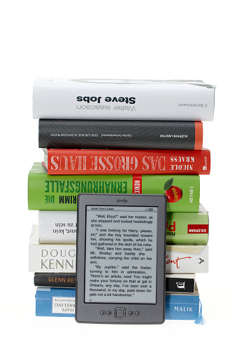 Hand holding e-reader in fornt of a pile of print books. Contemporary and traditional contrast. Selective focus.