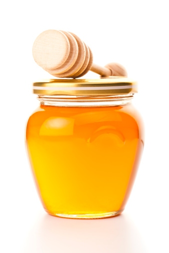 Jar of honey with honey dipper, isolated on white background.