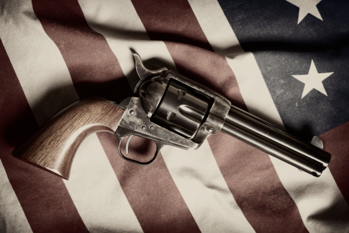 The legendary six-shooter from the Wild West, the Colt Peacemaker, sitting on top of an American flag.