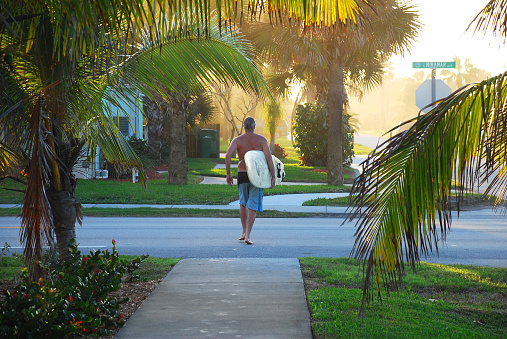 A man walks home from the beach after surfing in Indialantic, Florida