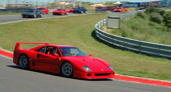 Zandvoort, The Netherlands - June 19, 2005: Two men driving a red Ferrari F40 around the Zandvoort race track during the Italia a Zandvoort days. Several other Ferrari cars are following in the background.
