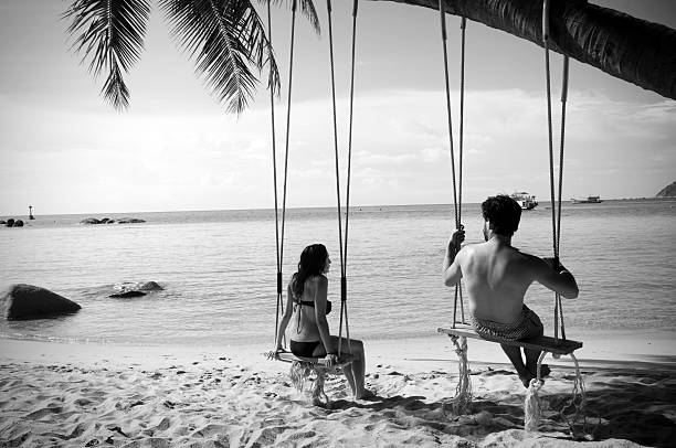 Black and white photo of a European couple sitting on rope swings at a beach in Ko Tao, Thailand