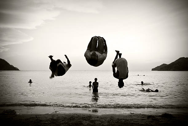 Teen age boy jumping on the beach at blue sea shore with his brother taking selfie with smartphone- Summer vacation