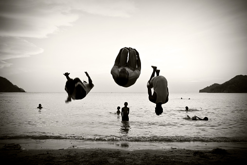 Black and white photograph of three young Colombians doing a flip together at the beach in Taganga, Colombia.