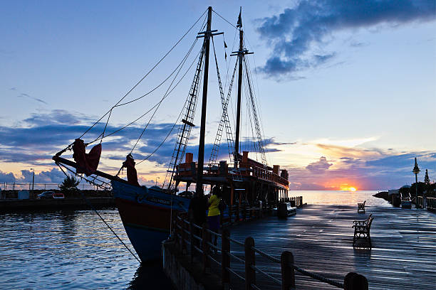 A striking silhouette of a historic sailing ship gliding across the sea at sunset. The golden hour light casts warm tones over the sky and water, while the glowing sun creates a dramatic contrast against the ship’s masts and rigging. A serene and atmospheric seascape capturing the timeless allure of maritime adventure.