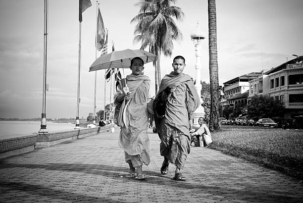 Buddhist monks in Phnom Penh, Cambodia Phnom Penh, Cambodia - June 25, 2007: Two Cambodian monks walk on a sidewalk that runs parallel to Preah Sisovath Boulevard. The building on the far right is the landmark Foreign Correspondence club; on the left is the Tonle Sap River. black and white travel travel destinations monk stock pictures, royalty-free photos & images