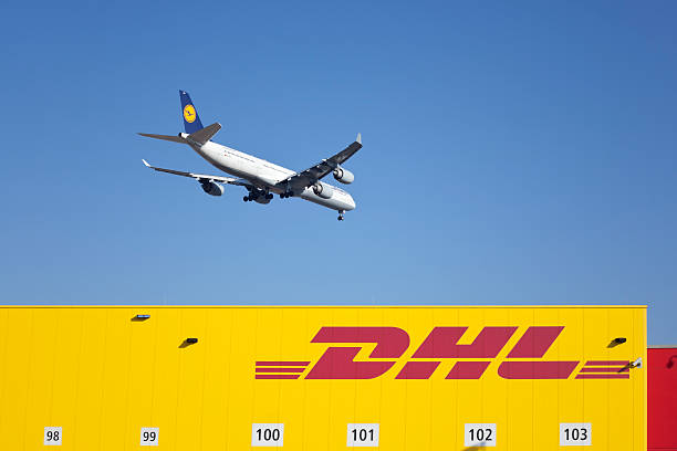 A DHL Boeing B767-3JHF(ER) plane, registration G-DHLE, taking off from Sydney Kingsford Smith Airport as flight HJ23 to Hong Kong.  The sun reflects brightly off the vertical stabiliser. This image was taken from New Link Road, Mascot on a hot and sunny afternoon on 11 October 2025.