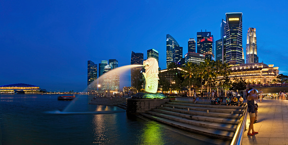 Singapore, Singapore - July 20, 2014: Tourist beside the Merlion statue fountain, iconic symbol of Singapore, overlooking the Marina Bay waterfront, the Esplanade Theatres, luxury hotels