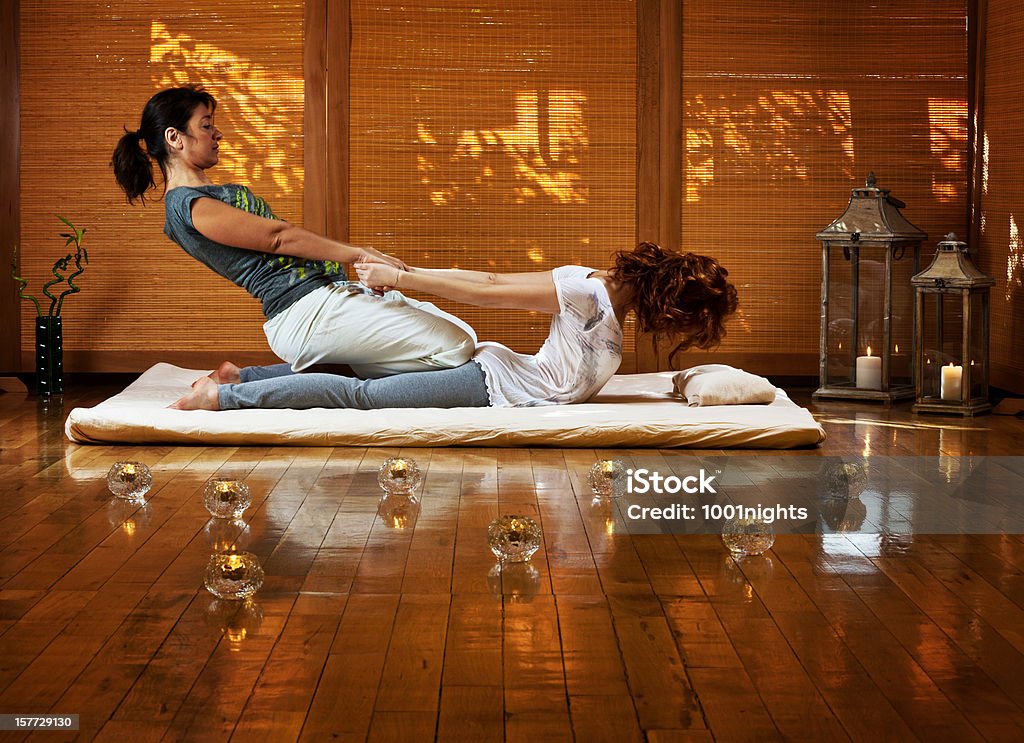 Thai massage Young female receiving massage by therapist in traditional thai position Massaging Stock Photo