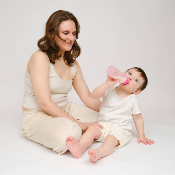istock Happy baby with mother drinks milk from bottle on studio white background. Resting child with mom eats formula. Kid about two years old (one year nine months) 1577302523
