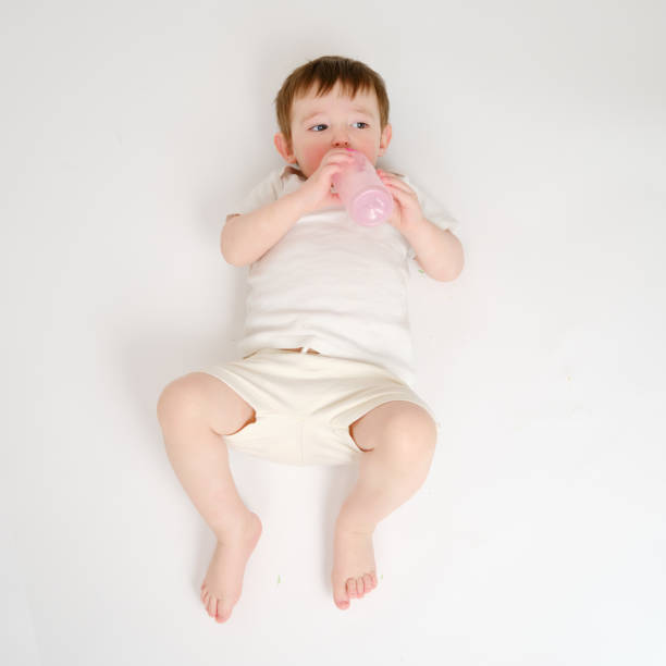 istock Happy baby drinks milk from bottle on studio white background. Resting child eats formula. Kid about two years old (one year nine months) 1577302524