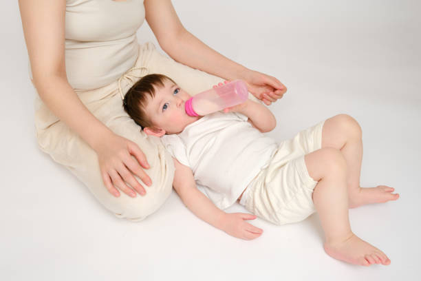 istock Happy baby with mother drinks milk from bottle on studio white background. Resting child with mom eats formula. Kid about two years old (one year nine months) 1577303045