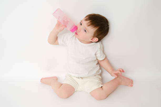 Happy baby drinks milk from bottle on studio white background. Resting child eats formula. Kid about two years old (one year nine months)