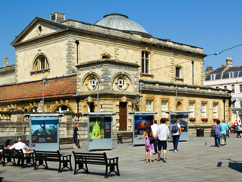 Close-up on a sign for the Bank of England, with pedestrians passing the institution's main entrance in the background.