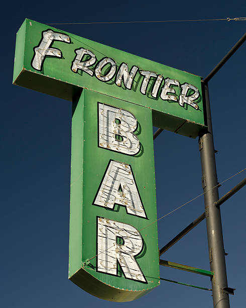 Las Animas, Colorado, Bent County, USA - May 31, 2024: Green corner building housing Fan Zone bar dominates a small-town street in Las Animas, Colorado. Eye-catching signage and colorful posters adorn the structure. Modest storefronts, utility poles, and parked vehicles surround it. Blue and overcast sky adds depth to this quintessential rural American scene.