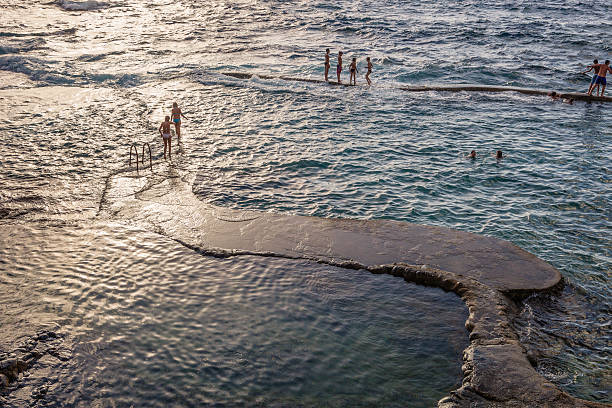 El Hierro, Spain - June 30, 2009: boys and girls standing at the edge of the pool, waiting for the waves crashing. These are the natural swimming pools of La Maceta, in the northern coast of El Hierro, a perfect place for swimming and having fun.