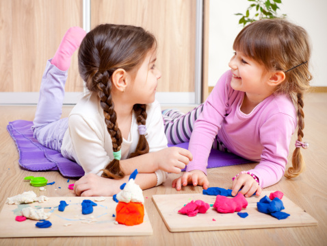 Two little girls are playing with plasticine.