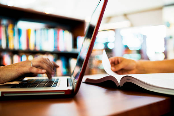 Laptop Computer and Book on Table Two people working with computer and book.Two people working with computer and book. textbook stock pictures, royalty-free photos & images