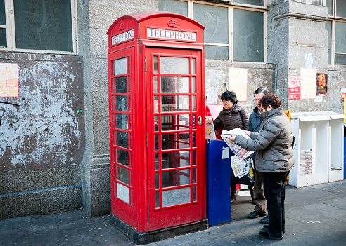 London, England- January 14, 2012: Free Chinese newspaper stand next to traditional English phone box. Chinese people reading THE Newspaper, taken in China Town, London - England.