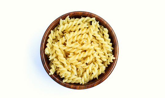 Fusilli pasta in a wooden bowl on white background top view