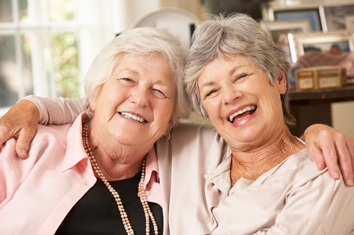 Portrait Of Two Retired Senior Female Friends Sitting On Sofa Smiling And Laughing with Each Other.