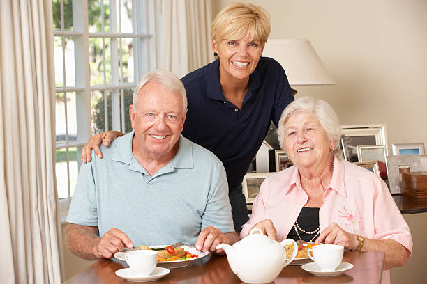 年配のカップルと一緒にお食事をお楽しみいただけるようお手伝いいたします。 - senior adult nursing home eating home interior ストックフォト�と画像