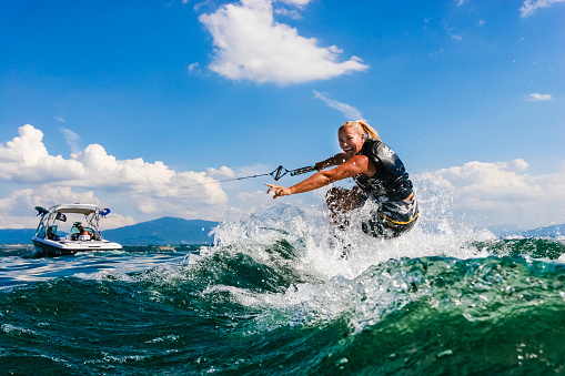 Portrait of a female wakeboarder smiling with pride because she successfully got up on the board. It is summer and there is bright sunlight. She is wake boarding on a lake and is wearing a lifejacket.
