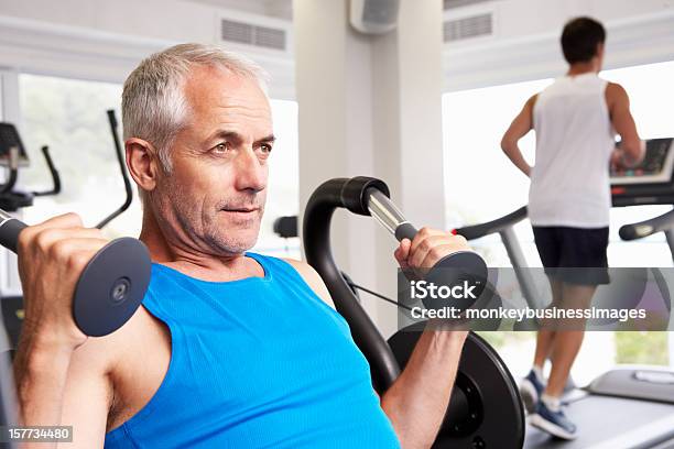 Man Using Weights Machine With Runner On Treadmill In Background Stock Photo - Download Image Now