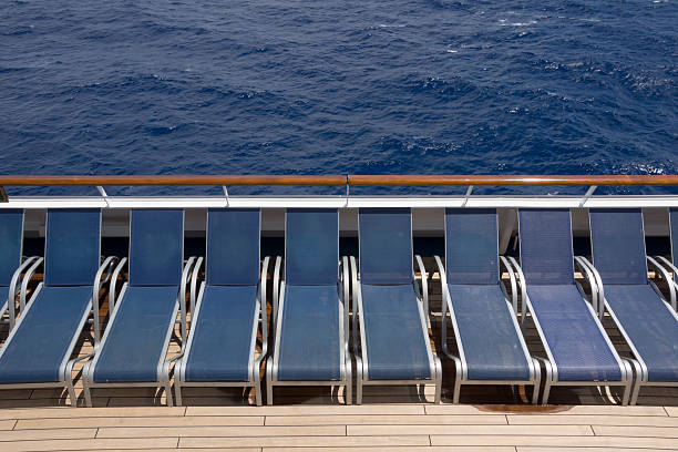 Raw of empty sun loungers on the deck of a cruise ship; behind them the blue ocean; copy space