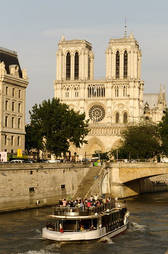 Paris, France - May 1, 2016: Notre Dame with people on the bank of Seine catching the spring sun in  Paris, France. The church dominates the image under a blue sky. Tiny people are seen on the bank by the water. Lunch green trees. A bridge in the background.
