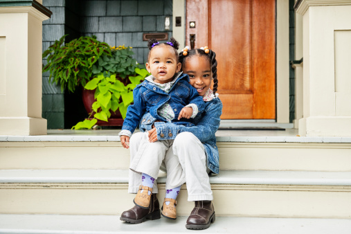 Portrait of two young sisters sitting on the steps of their front porch at home.