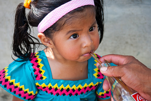 A local girl drinks Coca-Cola with a straw from a glass bottle in David, Panama