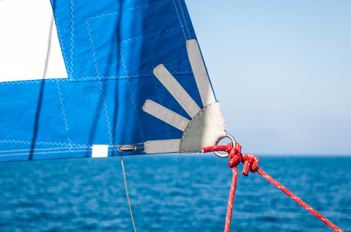 Close-up of a Red rope, knot and piece of sail on sailing boat floating on the blue water.