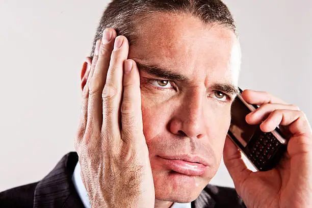 Close-up shot of a bored, frustrated businessman listening to something on his mobile phone - probably Greensleeves for the 50th time as he hangs on.