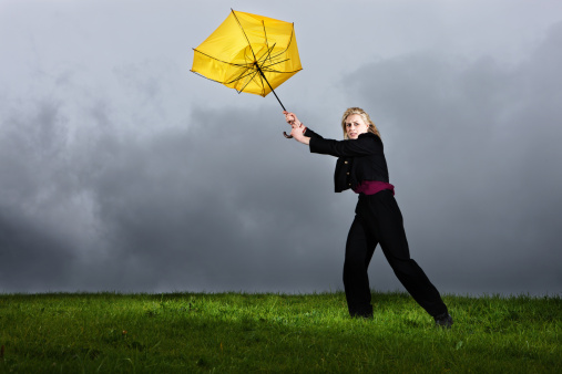 A pretty blonde woman hangs on helplessly to her frayed and broken umbrella as it blows away from her, dragging her along in a thunderstorm. 