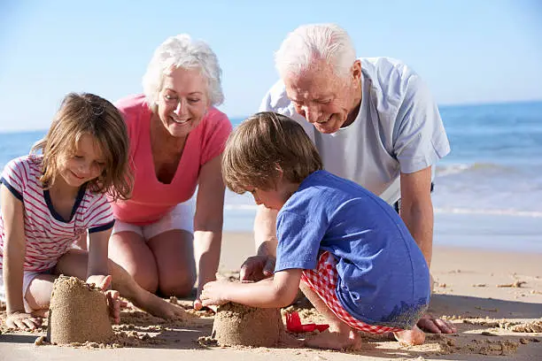 Smiling Grandparents And Grandchildren Building Sandcastle On Beach.