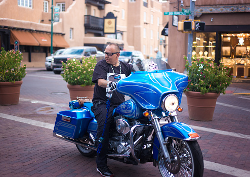 Santa Fe, NM: A man on a blue motorcycle on the historic Santa Fe Plaza.