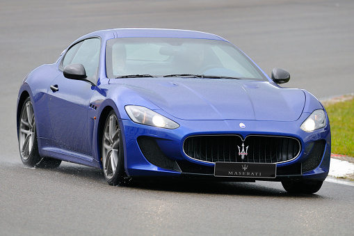 Zandvoort, The Netherlands - June 24, 2012: Blue Maserati GranTurismo sports car driving on a wet race track during the 2012 Italia a Zandvoort day. Two persons are sitting inside the car.