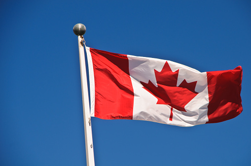The Canadian Flag flies in a stiff breeze on a flagpole in Quebec City against a deep blue cloudless sky