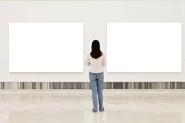 a woman in an art gallery looking at white frames - museum wall stockfoto's en -beelden